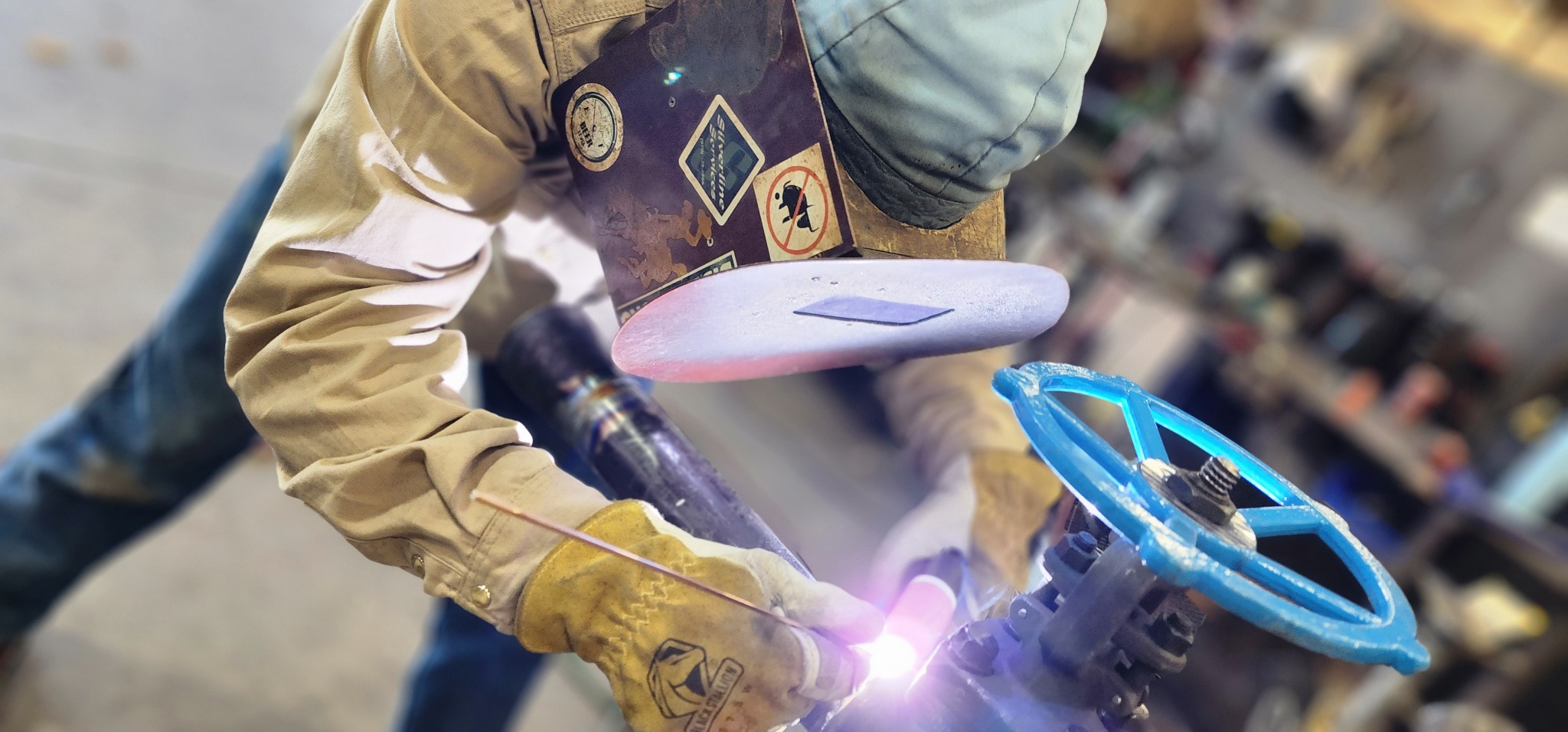 Field welder working on pipe near a valve handwheel